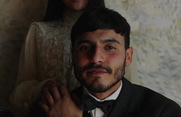 Portrait of a man in a suit and right behind his wife in a white dress and he looks at her