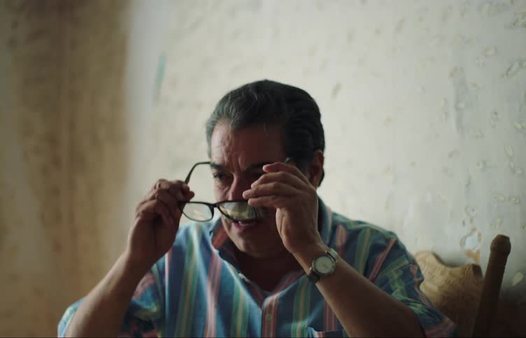 Man sitting in a chair wiping his nose and then putting on his prescription glasses