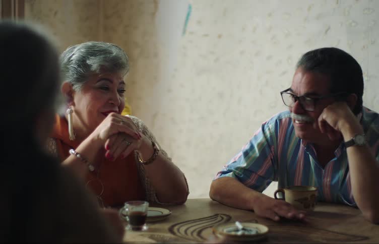 Elderly friends sitting at a table with cups of coffee and cigarettes smilingly talking to each other