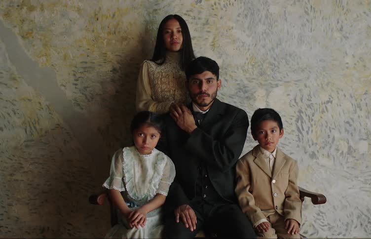 Portrait of a family of five seated together against a textured backdrop dressed in formal attire