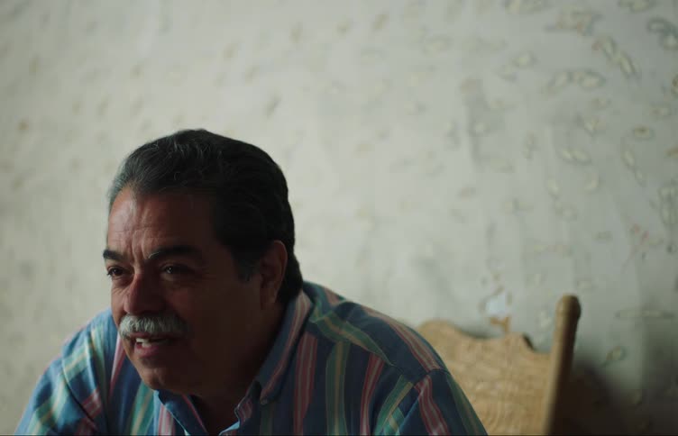 Older man sitting in chair indoors gestures while he talks