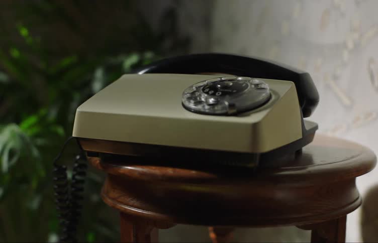 A vintage dial phone falls down from a shaking table