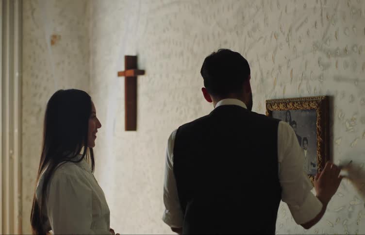 A man and a woman back to back are hanging a picture on a wall and then look at each other happily