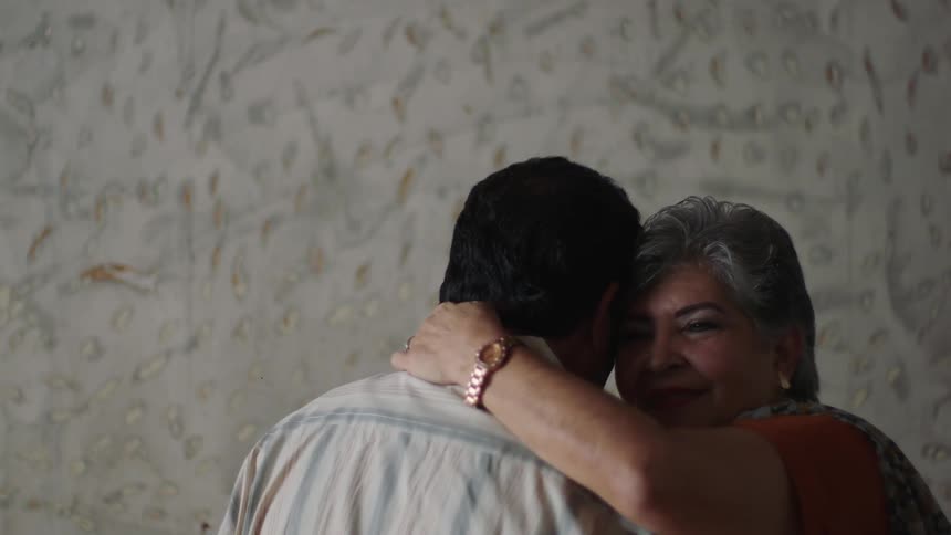 Older woman smiles while slow dancing with man in wallpapered room