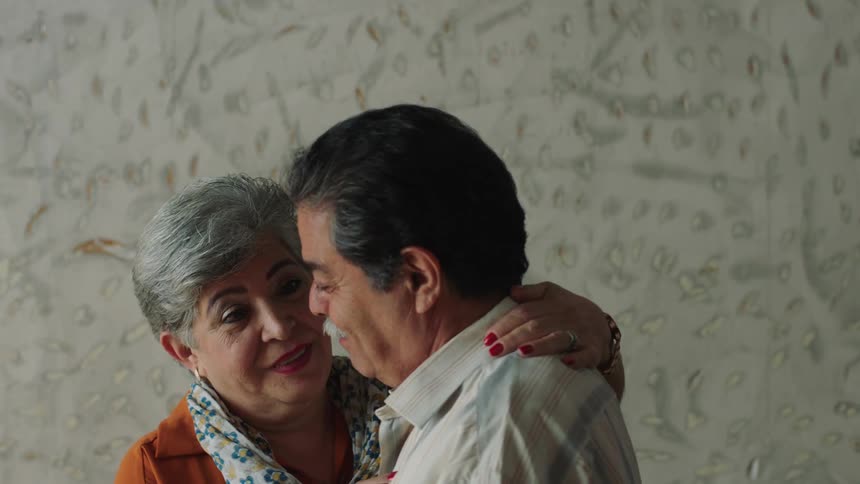 An elderly couple dancing in front of a textured wall