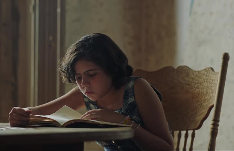 Girl sits at table while reading a book