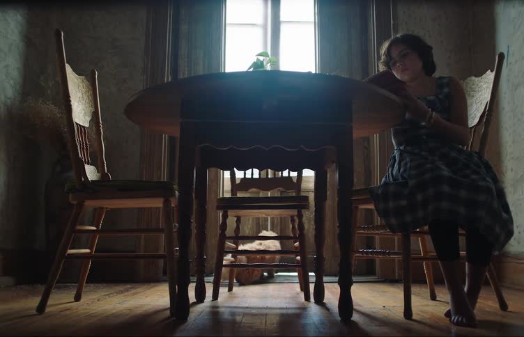A child is reading a book at the kitchen table next to her cat