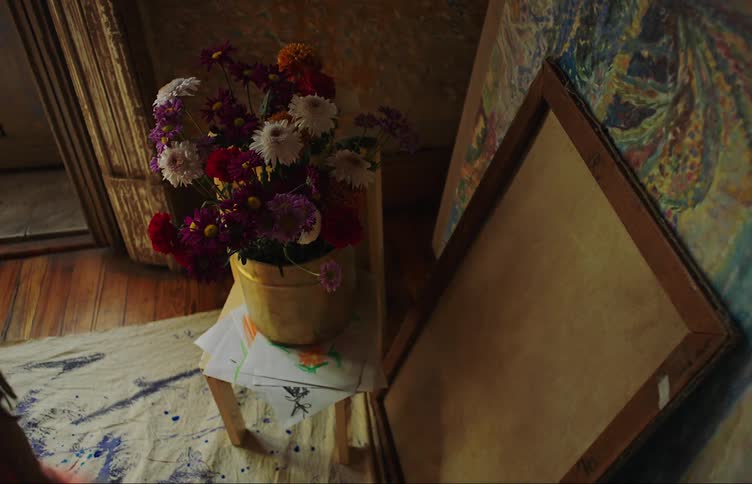 Womans hand picking a flower from a vase with colorful flowers next to frames with artistic paintings