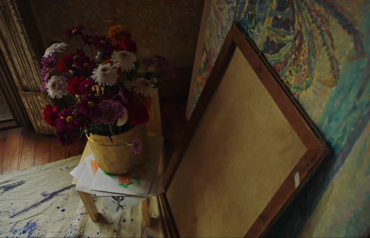 Vase of flowers on a small wooden table with artistic paintings next to it