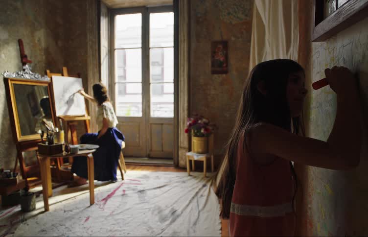 A child is drawing on a wall while a woman paints on a canvas near a window in a room with aged walls