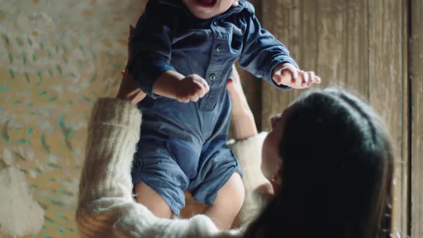 Mother throws her toddler into the air playfully and the child smiles