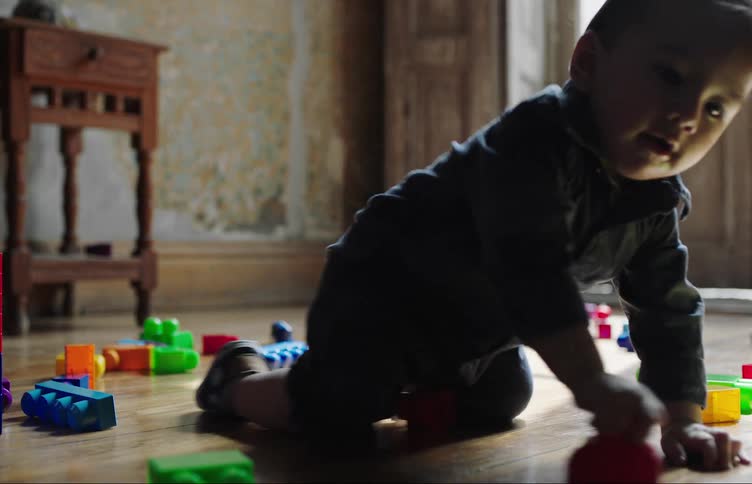A baby crawls across a wooden floor with scattered toy building blocks