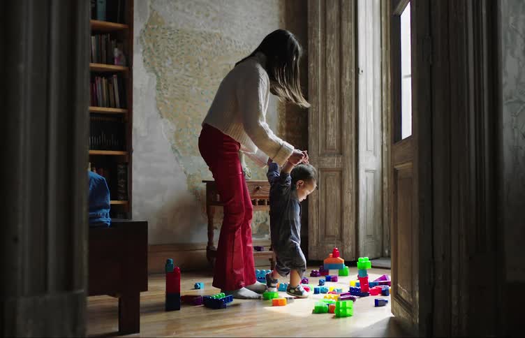 A mother helps her son walk over toys