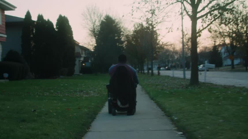 Person with the aid of an automatic chair walking along the sidewalk of a residential neighborhood