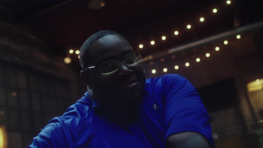 A black man dances happily in an old looking room with string lights