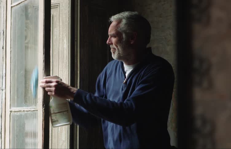 Older man cleans glass window with a rag and spray cleaner