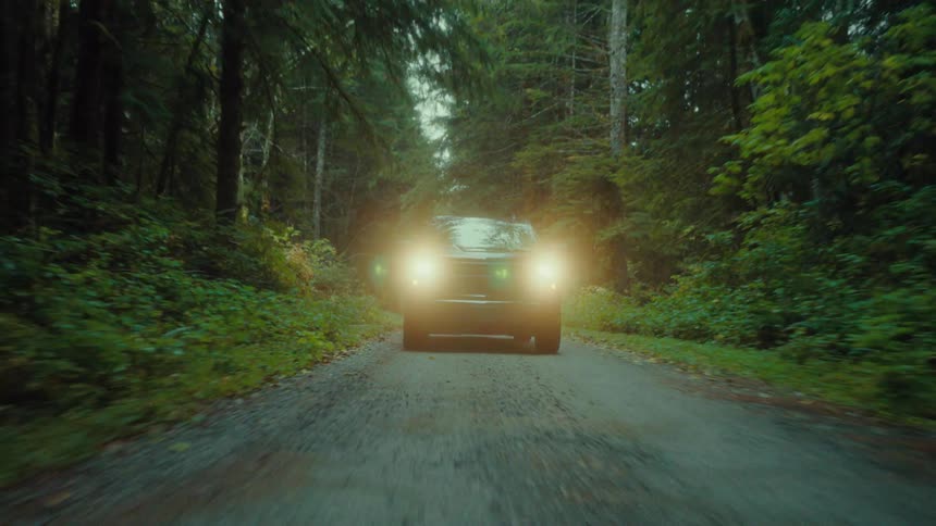 A black pickup truck with headlights on driving on a road through a forest