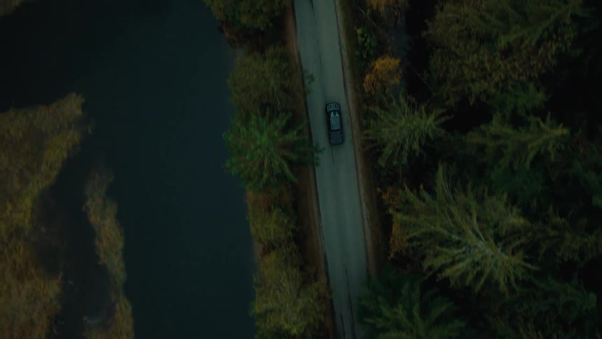 Aerial view of a car driving on a narrow road next to a river