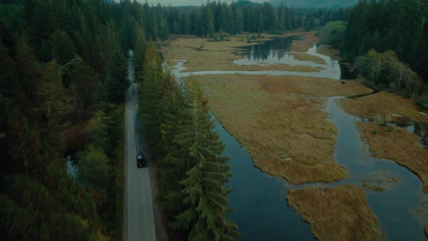 Aerial view tracking a black pickup truck driving near a river