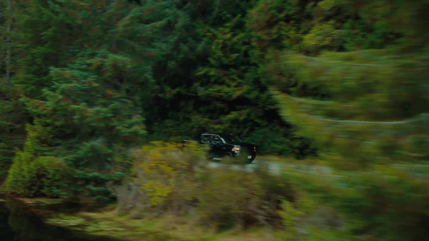 Aerial view of a black pickup truck driving through a forest