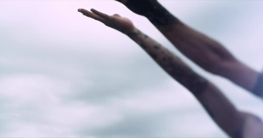Arms of a person with tattoo raising upwards on a cloudy day
