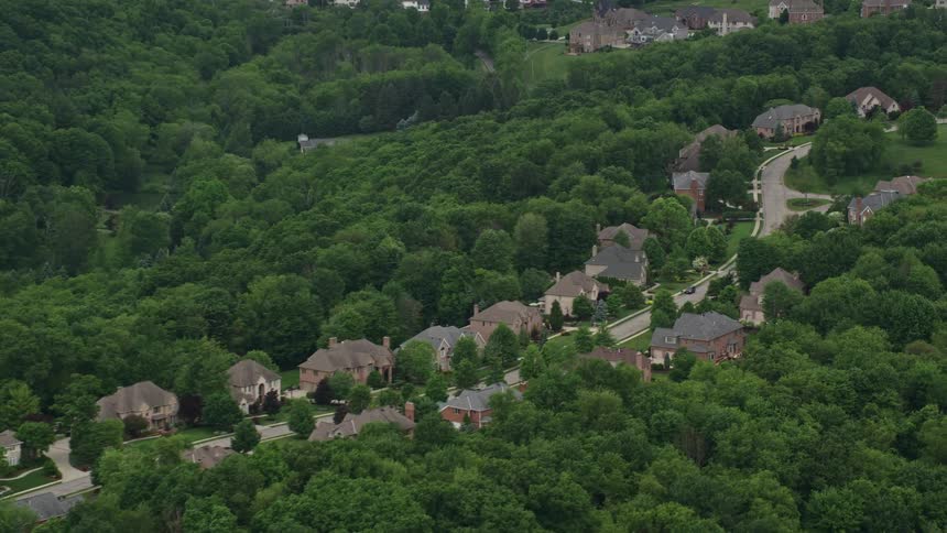 Aerial view of a residential area with houses amidst green trees and winding roads