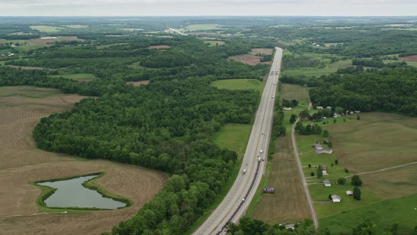 A highway with vehicles runs through a rural area with fields and ponds