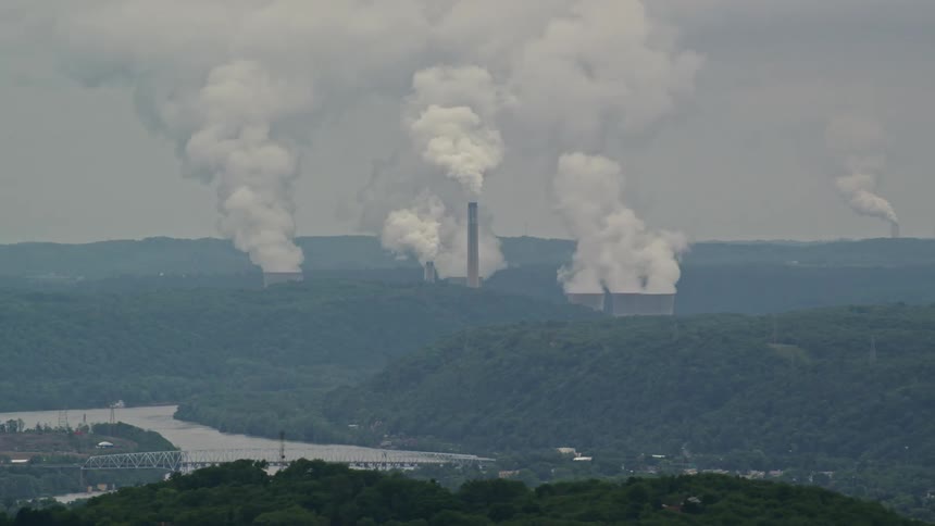 Large smokestacks emit clouds of smoke in a rural area