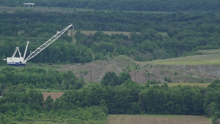 Large white crane in rural field towers over forest trees