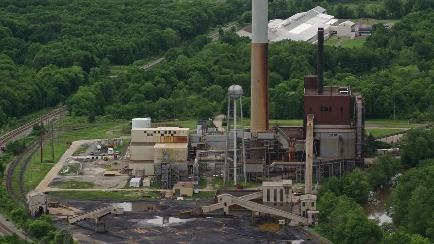 Aerial panorama of a factory with a chimney on the edge of a river and a railway line
