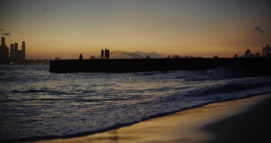 Sea landscape with waves at the edge of the sand and the silhouette of a metropolitan city in the background on a late afternoon with an orange sky