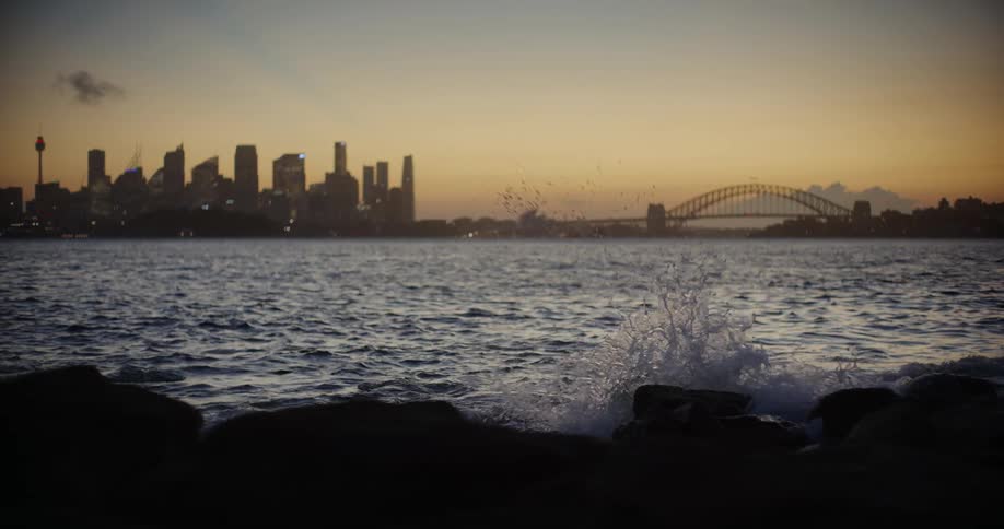 Panorama of a beach with calm waves in a reddish morning sky and the silhouette of a metropolis with a skyscraper on the horizon
