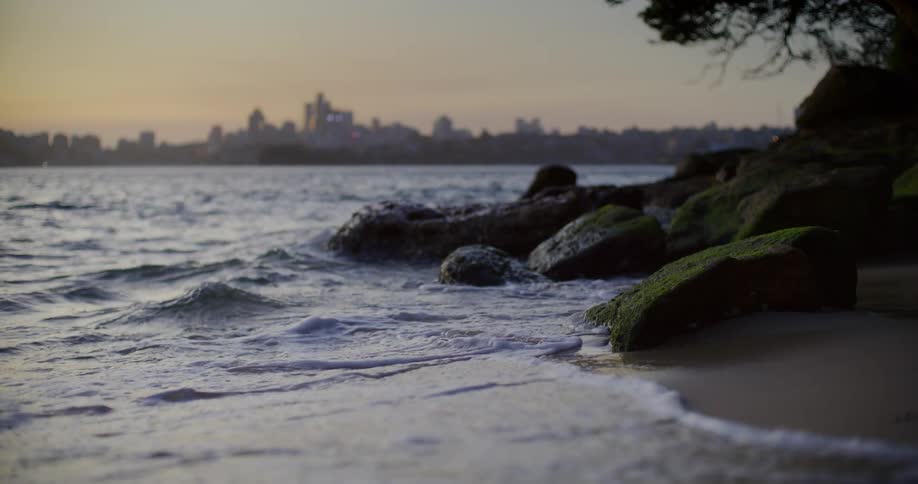 Ocean water is crashing towards the beach coast at dusk