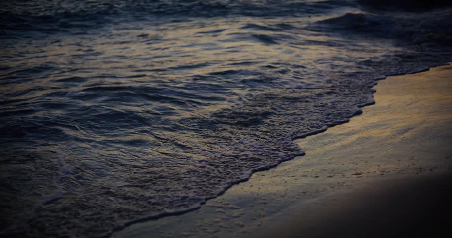 Waves crashing on sandy shoreline at sunset