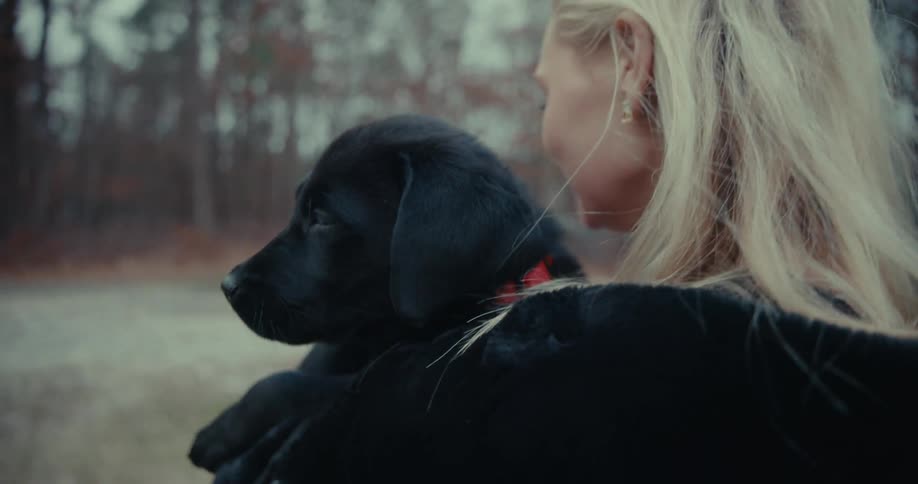 A young woman carries her puppy outside