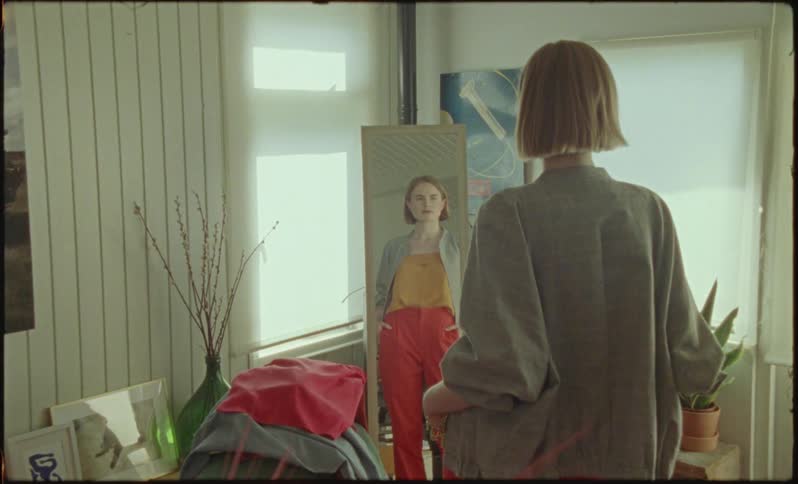 A woman stands still in front of a mirror