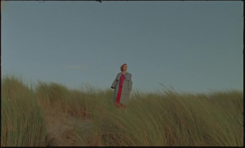 A woman wearing a coat stands on a beach