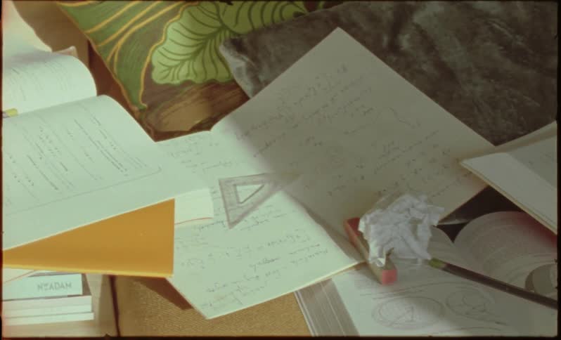 Open school books are scattered on a bed with a crumpled paper in the middle