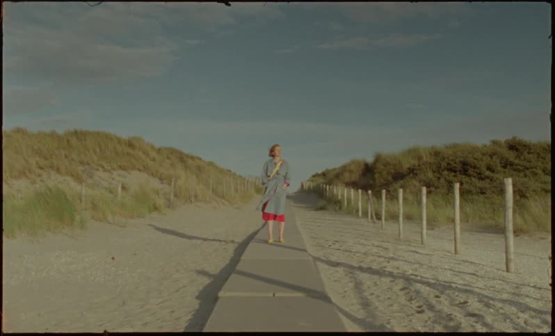 A white woman stands on a walkway on a beach