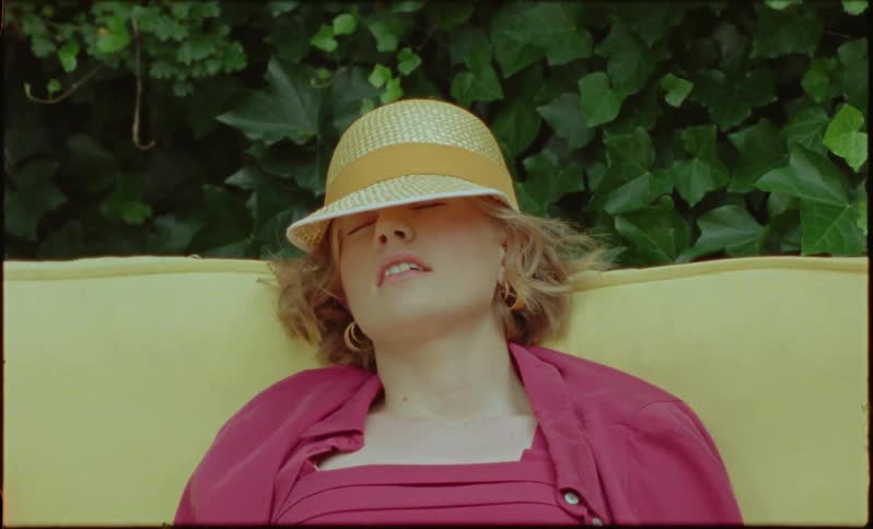 Woman is napping outdoors on a surface near plants