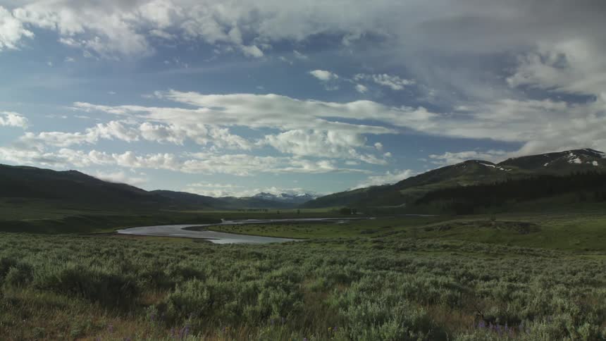 A river valley surrounded by mountains with blue sky day and clouds