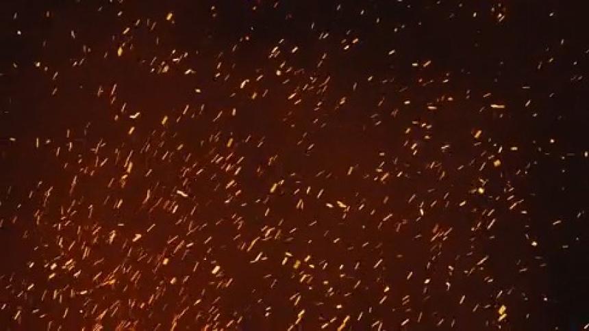 Embers of burning fire with smoke rising across the dark night sky
