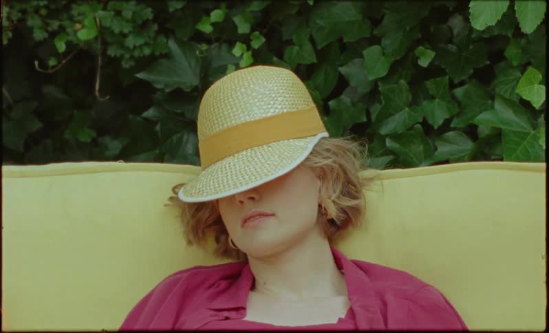 A woman sitting outdoors with a hat covering half of her face