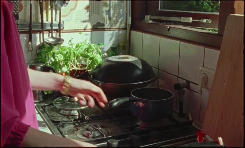 A womans hands on the stove in her home placing vegetables and a pan with steam coming out