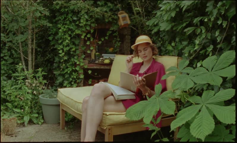 Young woman sitting in a garden reading a book and taking notes