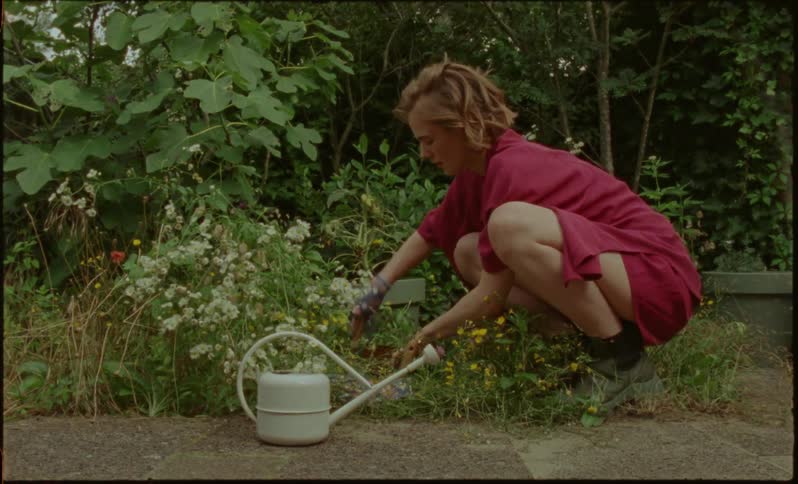 A young woman in a red dress uses a trowel to dig out soil in a flower garden