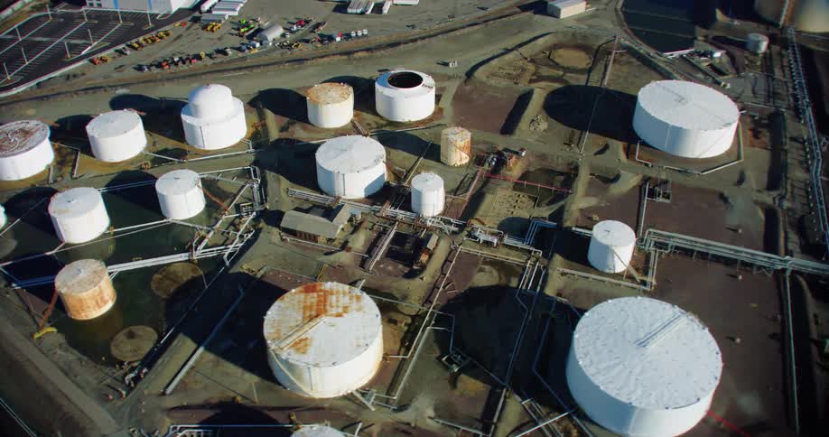 Multiple tanks of various sizes stand across from warehouse and other buildings