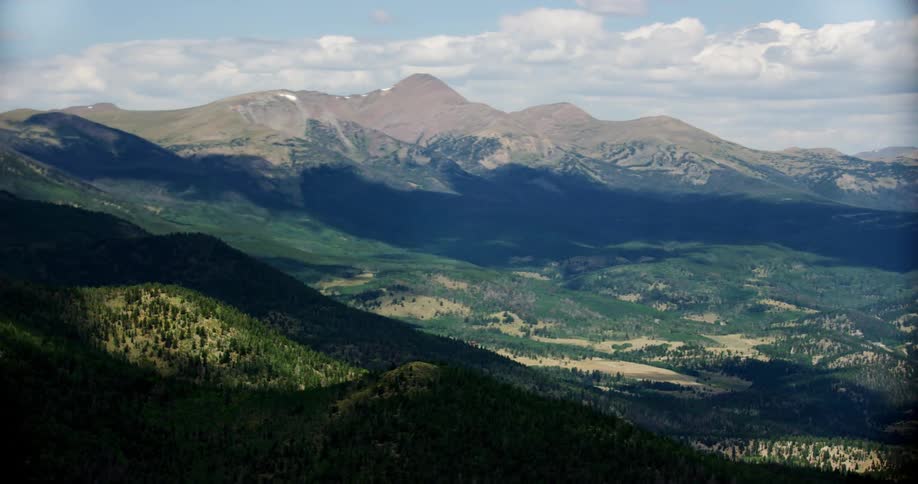 Aerial panorama of mountain ranges on greenish hills with forests on a blue sky day with clouds