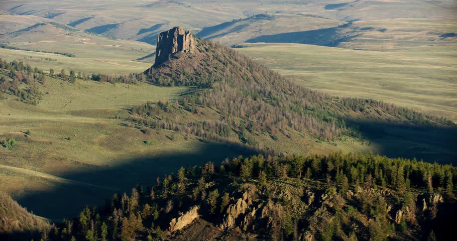Stone and forest covered hills sit on grass covered hilly terrain