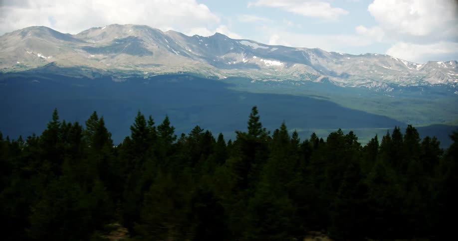 A mountain range towers over plains and a pine forest